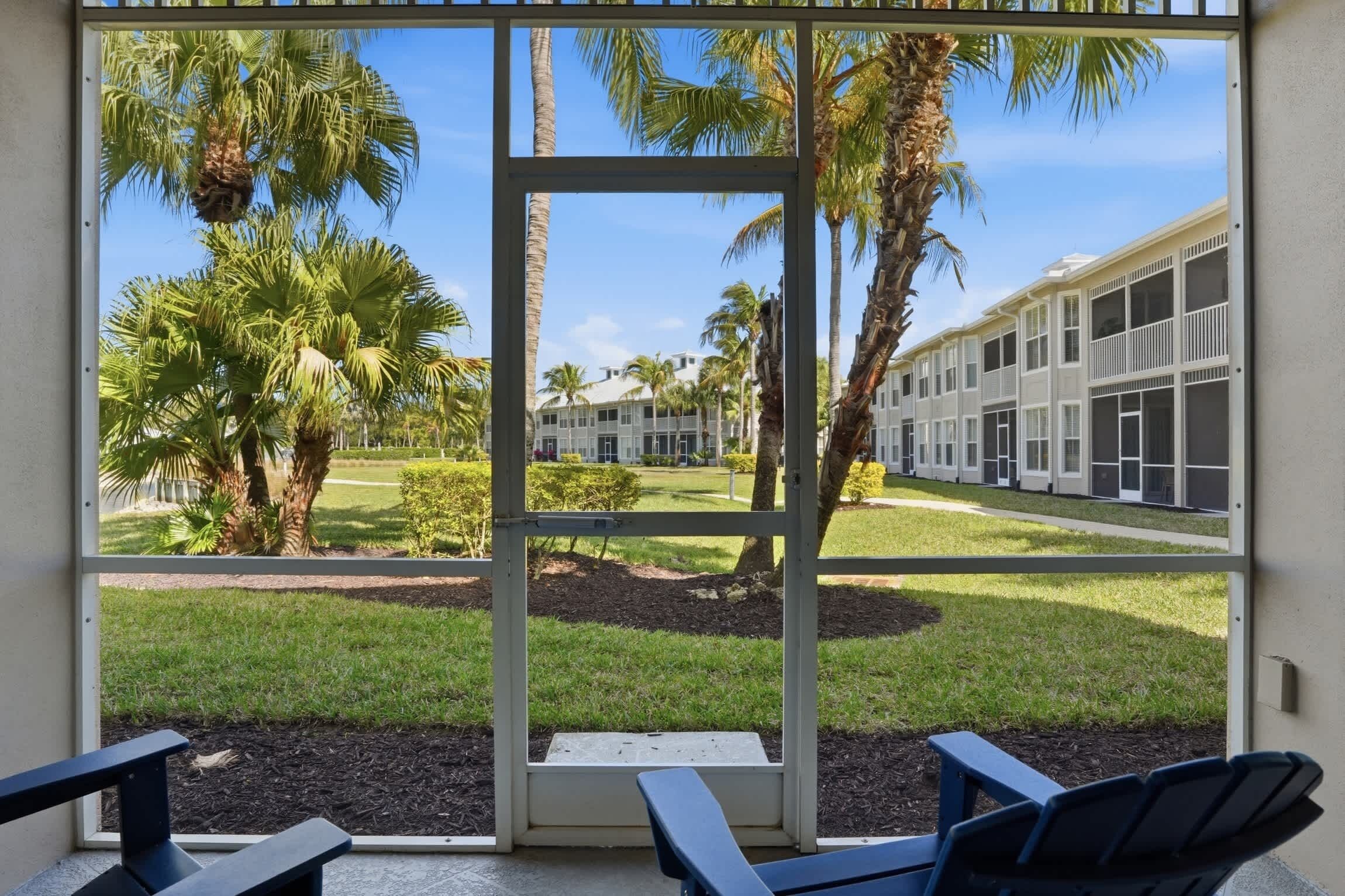 A view through a glass door of a building with palm trees and a lawn.