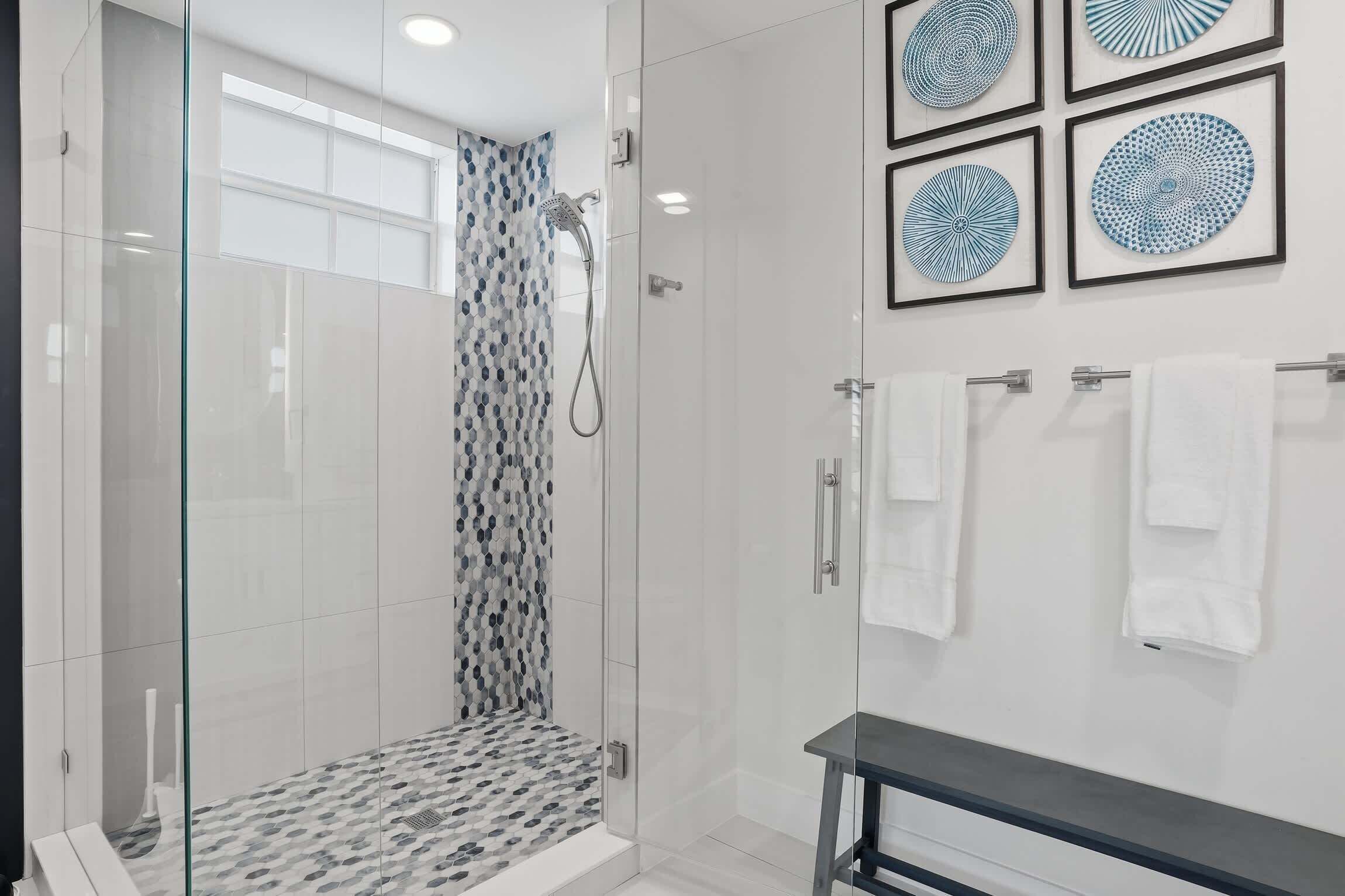 A modern bathroom with a glass-enclosed shower, white tiled walls, and framed wall art.