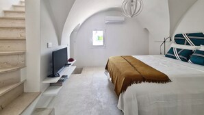 Un dormitorio moderno con techo inclinado, una cama con manta marrón, un televisor en una estantería y una ventana con vistas.