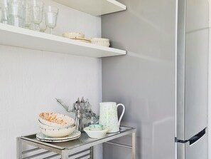 A kitchen with a stainless steel refrigerator, a glass shelf with dishes, and a metal table with bowls and utensils. - A Casa di R by Wonderful Italy (Ostuni)
