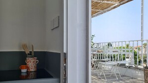 Puerta abierta a un balcón con una parrilla, una taza y utensilios sobre la encimera.