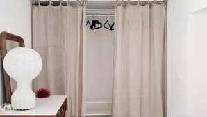 Una habitación con un aparador de madera, un espejo, una lámpara blanca y un armario con ropa colgada.
