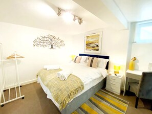 Ein ordentlich eingerichtetes Hotelzimmer mit einem Bett, Nachttischen, einem Schreibtisch, einem Stuhl, einer Garderobe und einem Wandbild.