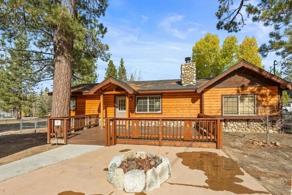A wooden lodge with a stone fireplace, wooden deck, and a stone chimney. - Log Cabin Dream (Big Bear Lake)