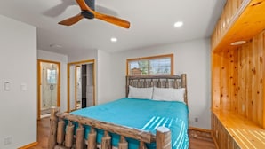 Une chambre à coucher avec un lit en bois, un ventilateur de plafond, une fenêtre avec des stores et un banc en bois.