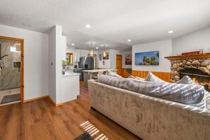 A modern living room with a sofa, a fireplace, and a kitchen in the background. - Log Cabin Dream (Big Bear Lake)