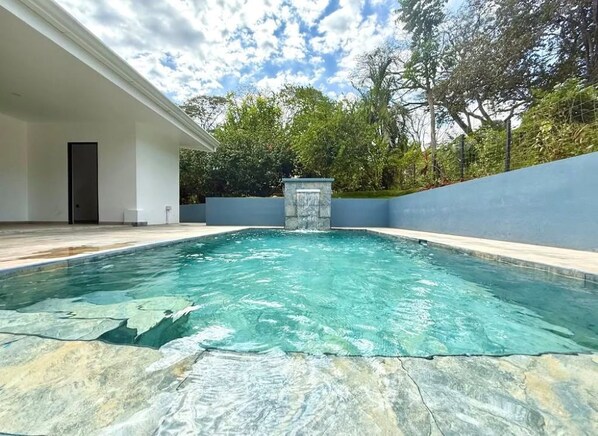 Una piscina con cubierta de piedra, rodeada por un muro bajo y árboles.