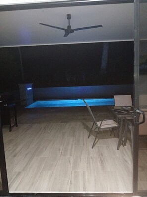 Una habitación con ventilador de techo, una pequeña mesa con sillas y una zona iluminada en azul.