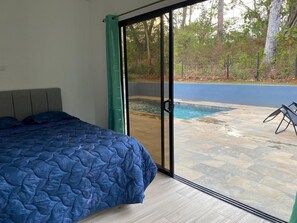 Un dormitorio con cama y puerta corrediza a un espacio exterior con piscina.
