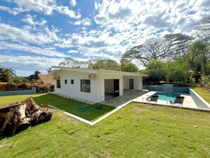 Una casa moderna con piscina, césped cuidado y un árbol grande al fondo.