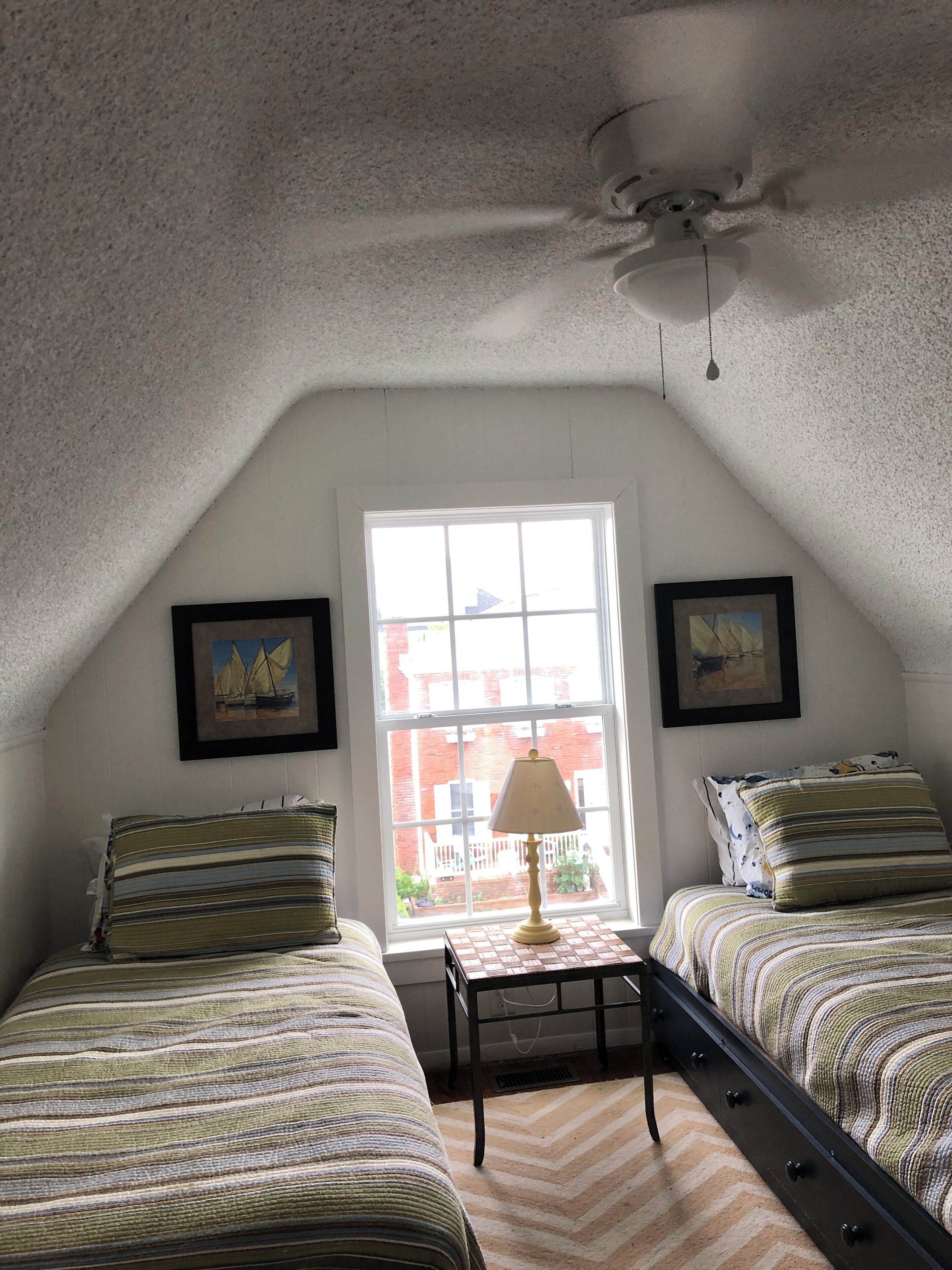 Ein Schlafzimmer mit zwei Betten, einem Deckenventilator, einem Fenster mit Aussicht und zwei gerahmten Bildern an der Wand.
