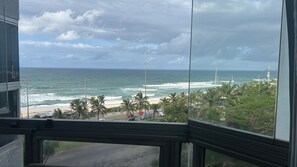 Vista del océano desde una ventana con vista a una playa con palmeras y una carretera.