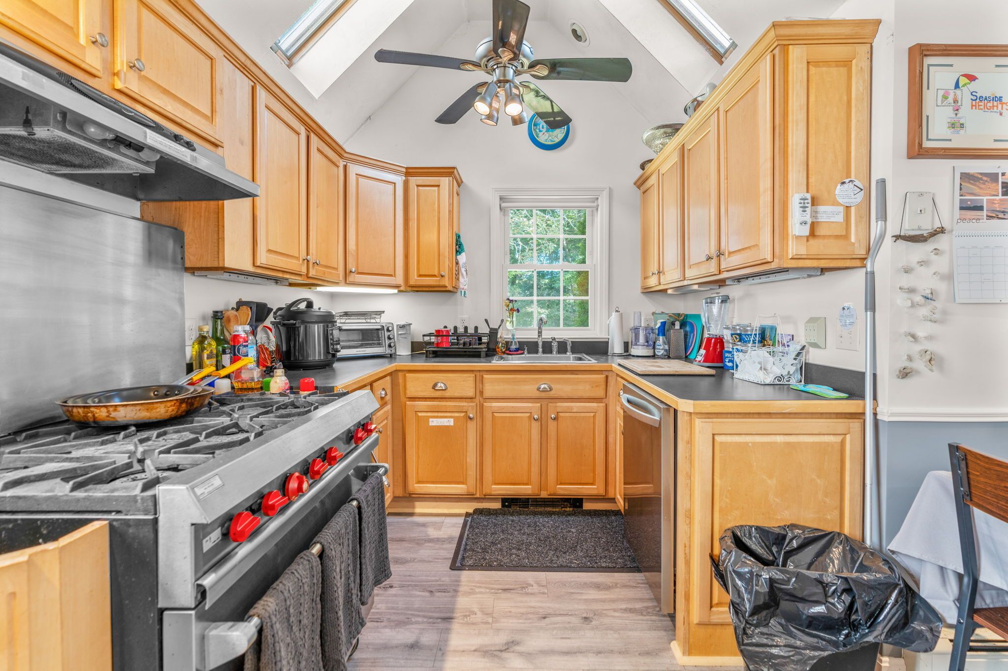 A kitchen with wooden cabinets, a gas stove, a ceiling fan, and a window.