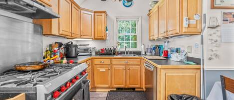 A kitchen with wooden cabinets, a gas stove, a ceiling fan, and a window.