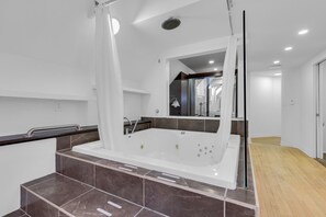 A modern bathroom with a large bathtub, a shower area, and a mirror. - Maison Paris (Montréal)
