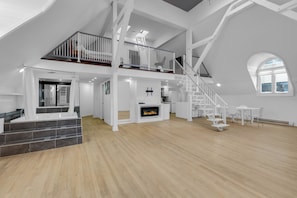 A spacious loft with a high ceiling, a fireplace, a staircase, and a balcony. - Maison Paris (Montréal)