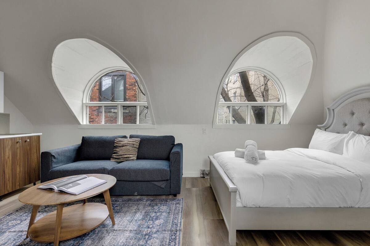 Un dormitorio con una cama, un sofá, una mesa de centro y dos ventanas de arco.