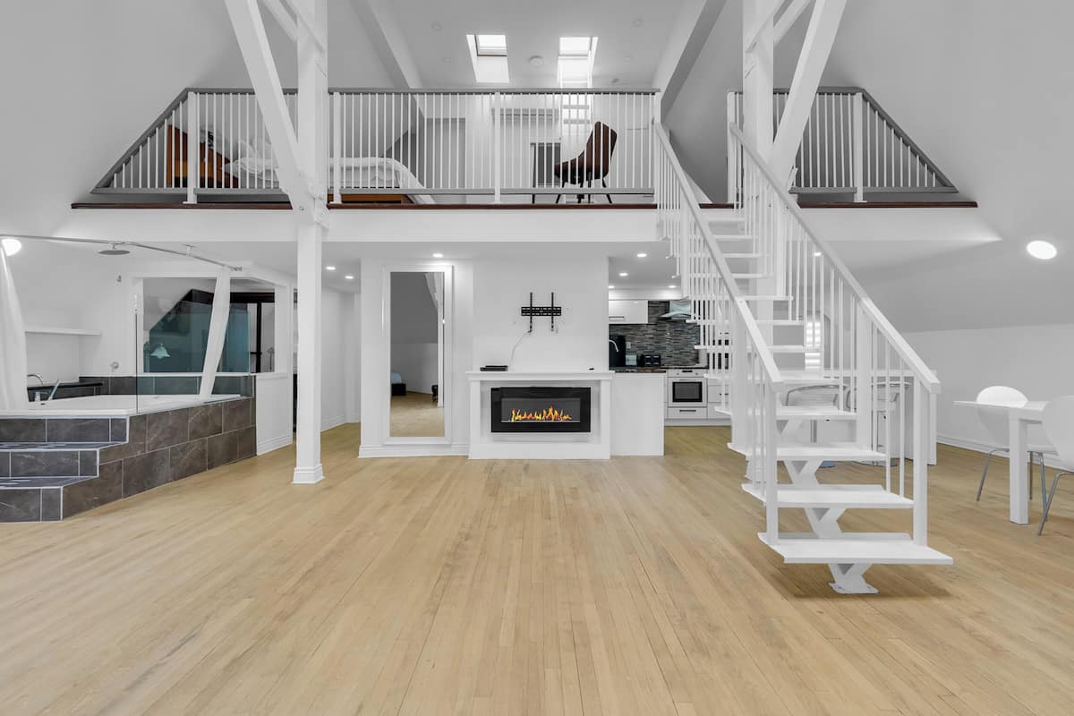 Un loft espacioso con techo alto, chimenea, escalera y zona de comedor.
