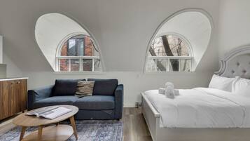 A bedroom with a bed, a sofa, a coffee table, and two arched windows.