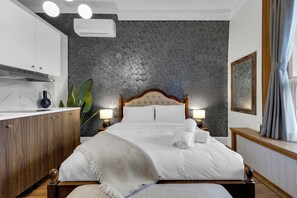 A neatly arranged hotel room with a bed, bedside lamps, a wooden nightstand, a mirror, and a large window with curtains. - Maison Paris (Montréal)
