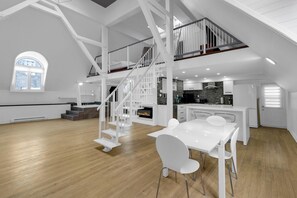Un amplio espacio de estar con una escalera blanca, una mesa de comedor y una zona de cocina.
