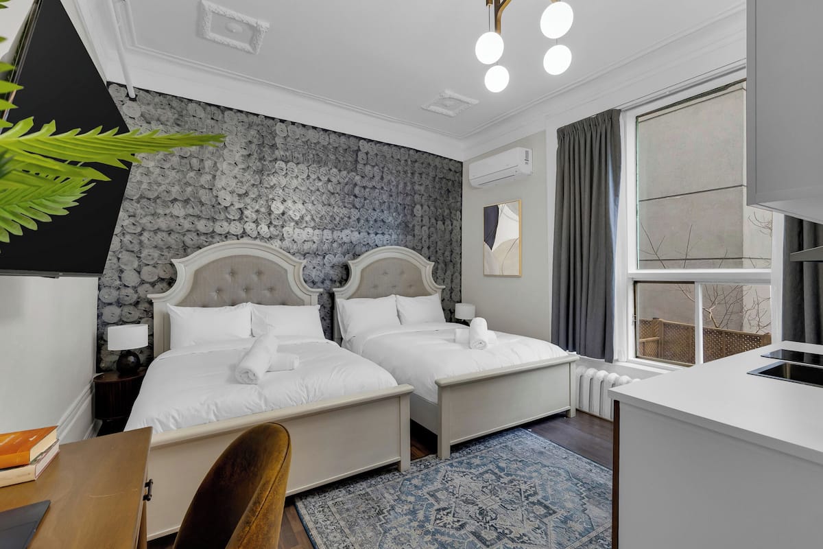 Habitación de hotel con dos camas, un escritorio, una silla, un ventanal grande y una pared con diseño.