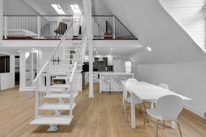 A spacious loft with a high ceiling, a central kitchen area, and a dining space with white furniture. - Maison Paris (Montréal)