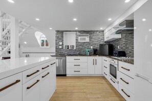 A modern kitchen with white cabinetry, a stainless steel dishwasher, a microwave, and a built-in oven. - Maison Paris (Montréal)