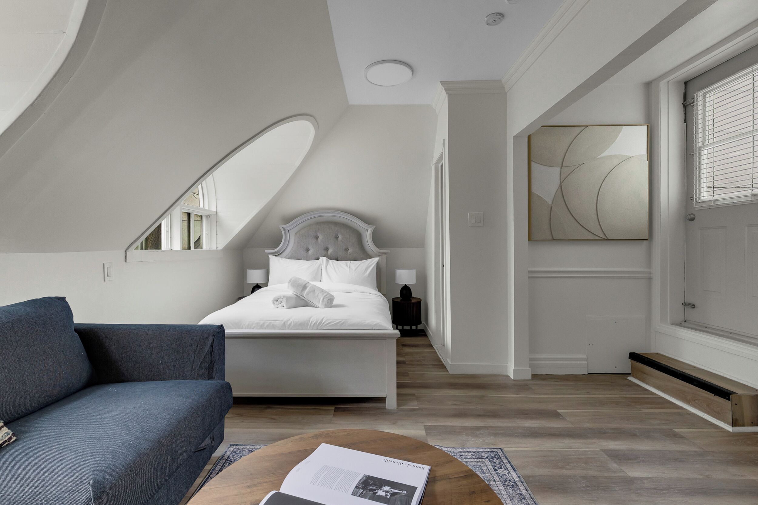 Een slaapkamer met een bed, een bank, een bijzettafeltje en een groot raam.