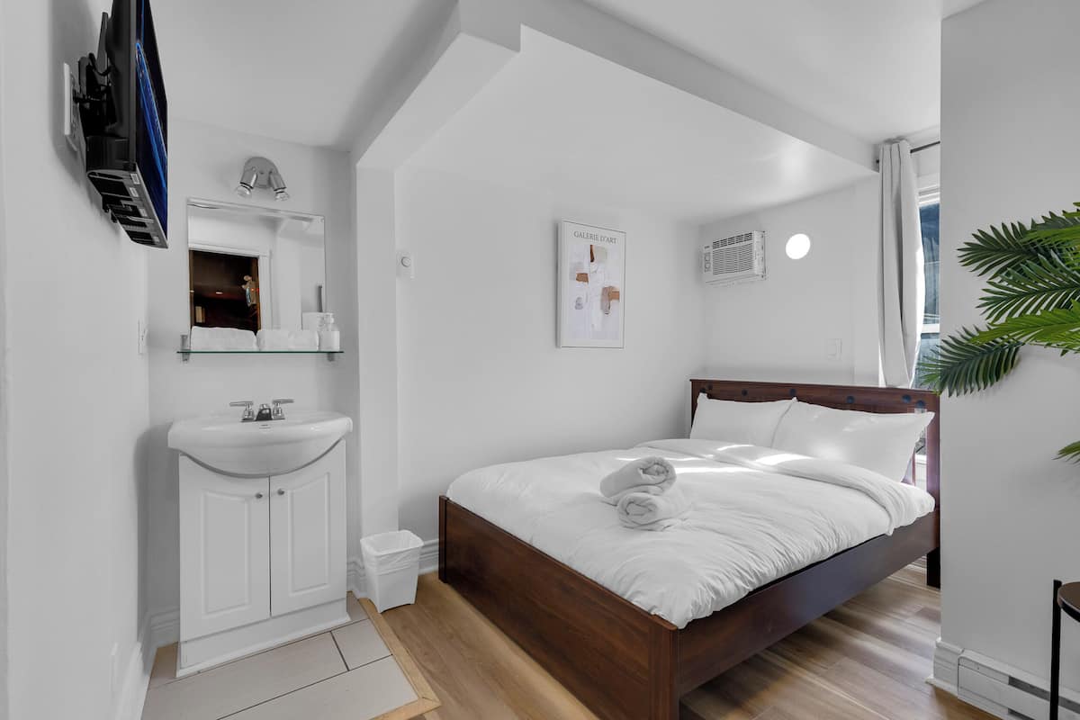 Un dormitorio con cama de madera, ropa de cama blanca, un lavabo blanco y un espejo.