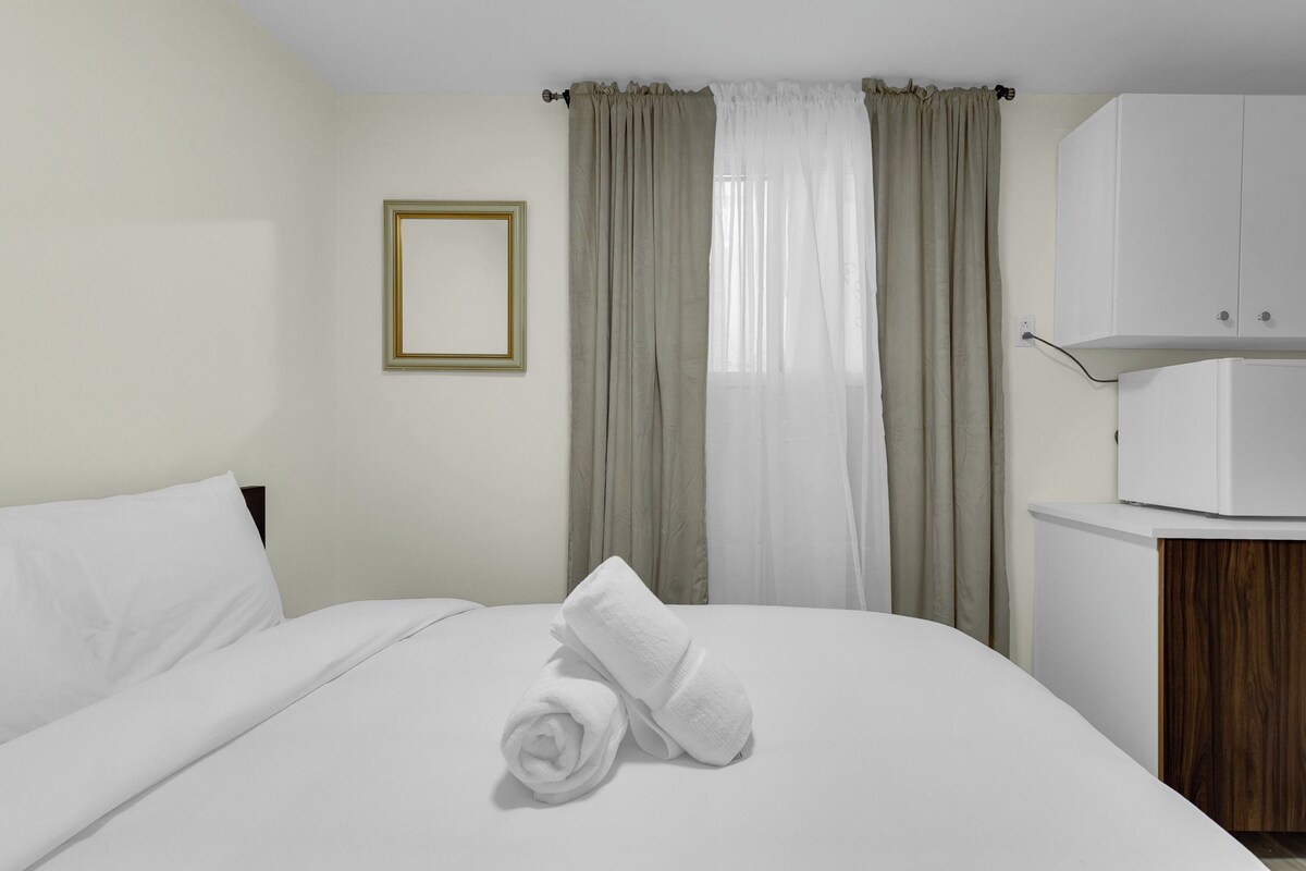 A hotel room with a neatly made bed, a bedside table with a lamp, a wardrobe, and a framed picture on the wall.