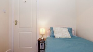 A bedroom with a single bed, a bedside table with a lamp, and a white door. - 7 Erme Drive (Ivybridge)