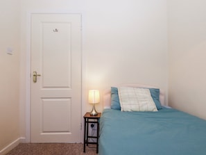Ein Schlafzimmer mit einem Einzelbett, einem Nachttisch mit Lampe und einer weißen Tür.