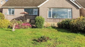 A two-story house with a tiled roof, a large window, and a small patio with a table and chairs. - 7 Erme Drive (Ivybridge)
