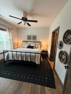 Een slaapkamer met een bed, plafondventilator, bedlampjes en decoratieve wandkunst.
