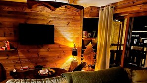 Interior acollidor d'una cabana amb una paret de fusta, una televisió, una taula petita amb una làmpada i un sofà.