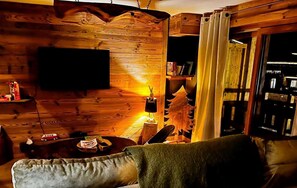 Ein gemütliches Blockhaushaus-Interieur mit einer Holzwand, einem Fernseher, einem kleinen Tisch mit Lampe und einer Couch.