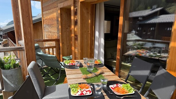 Una terrassa de fusta amb mobiliari exterior, una taula de buffet plena d'aliments i vista a un edifici tradicional.