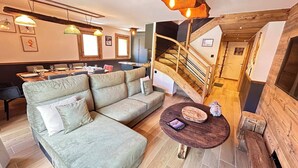 Un interior modern amb un sofà, zona de menjador, escala i detalls de fusta.