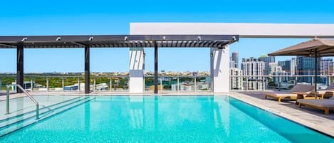 A rooftop pool with a city view, a pergola, and lounge chairs.