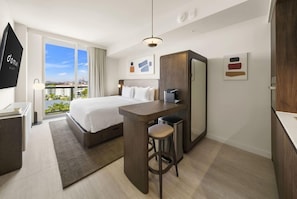 A hotel room with a bed, a desk with a chair, a large window with a view, and a flat-screen TV. - Urban Studio | Domus Brickell (Miami)
