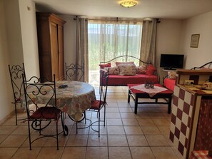 Ein Zimmer mit Esstisch, Stühlen, einer Couch, einem Fernseher und einer kleinen Küchenzeile.