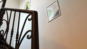 Una escalera con barandillas metálicas decorativas, una pared lisa con dos cuadros enmarcados y una lámpara en el techo.