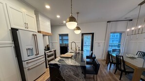 A modern kitchen with white cabinetry, a marble island, and a dining area with a view. - Harbor Lights Resort Waterfront Pool Dock (Oak Island)