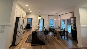 A modern kitchen with white cabinets, a dining area with a table and chairs, and a large window providing natural light. - Harbor Lights Resort Waterfront Pool Dock (Oak Island)