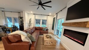 A modern living room with a brown leather sofa, a wooden coffee table, a fireplace, and a ceiling fan. - Harbor Lights Resort Waterfront Pool Dock (Oak Island)