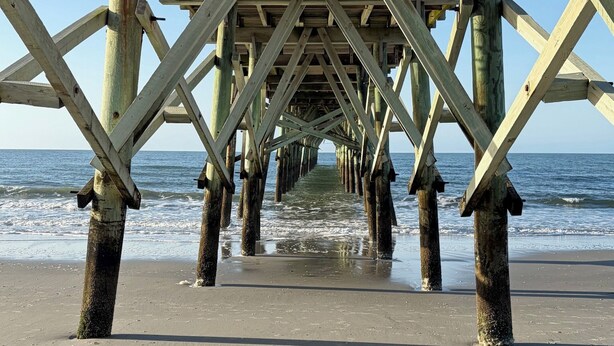 A wooden pier structure with a clear view of the ocean and sandy beach. - Harbor Lights Resort Waterfront Pool Dock (Oak Island)