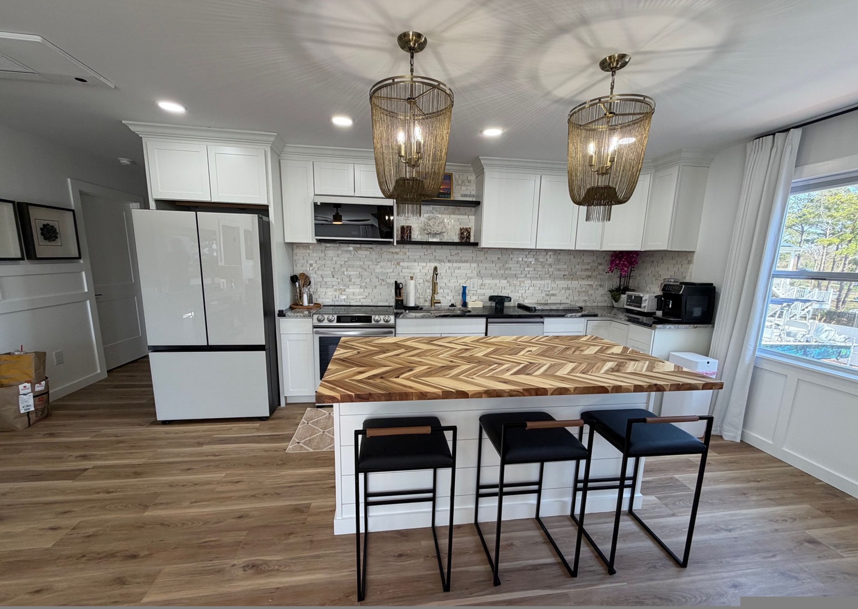 A modern kitchen with white cabinetry, a wooden herringbone countertop, and black bar stools.
