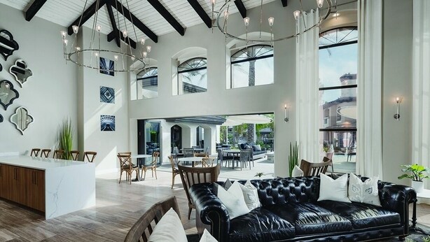 Een ruime woonkamer met een zwarte leren bank, houten stoelen, een salontafel en een keukeneiland.