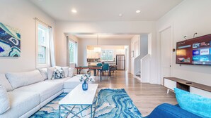 A modern living room with a sofa, coffee table, and TV. There is a kitchen in the background with a dining area. - Quiet Charlotte Home, Sleeps 8, Near Uptown (Charlotte)